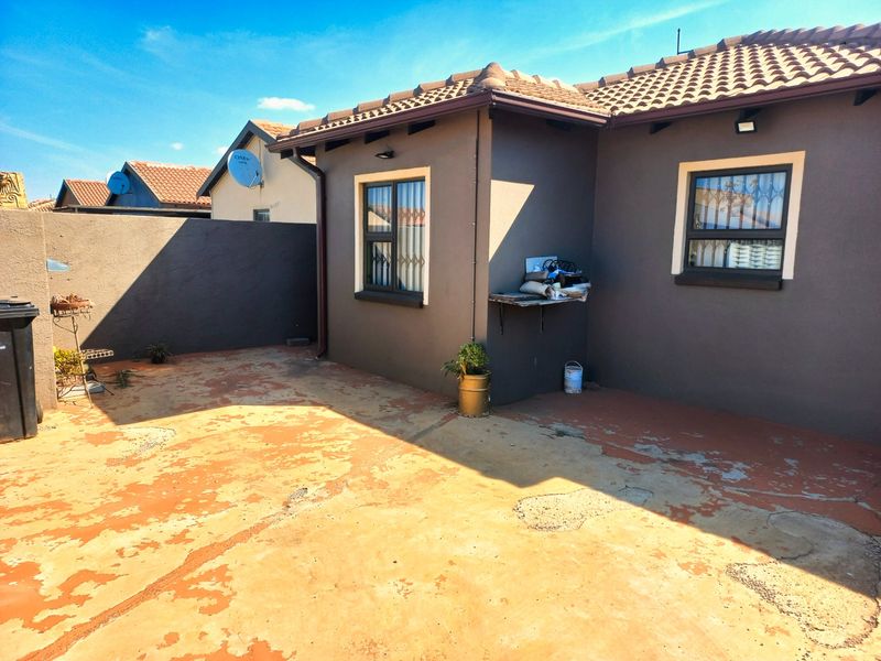 Rear exterior view of the property featuring a paved patio area, tiled roof, and security bars on the windows.