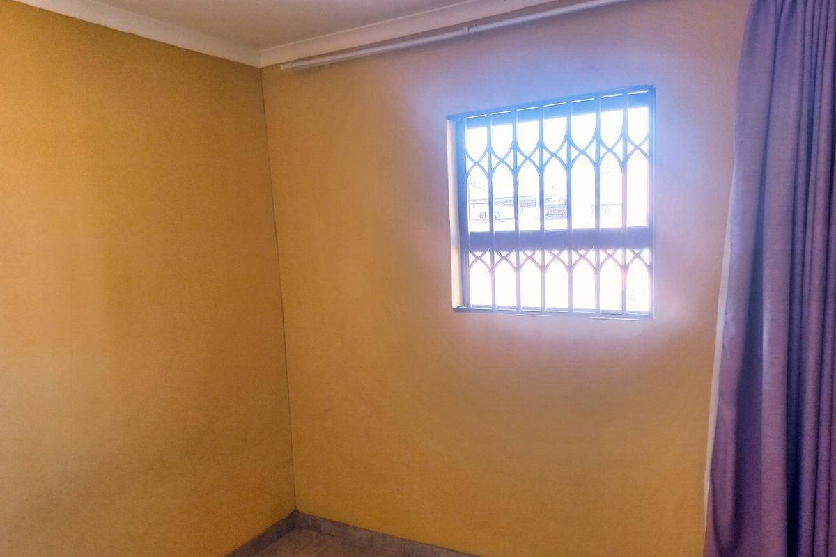 An empty bedroom featuring tiled flooring, yellow painted walls, and a window fitted with a security gate.