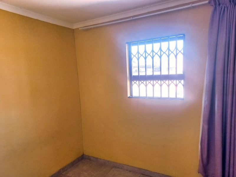 An empty bedroom featuring tiled flooring, yellow painted walls, and a window fitted with a security gate.