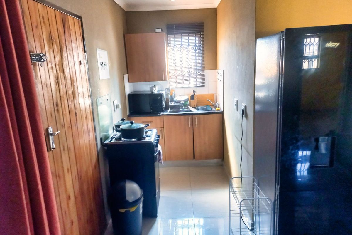 A compact kitchen featuring built-in cabinetry, tiled flooring, and a functional sink area with security bars on the window.