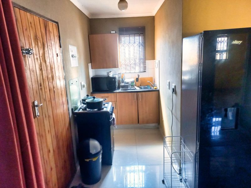 A compact kitchen featuring built-in cabinetry, tiled flooring, and a functional sink area with security bars on the window.