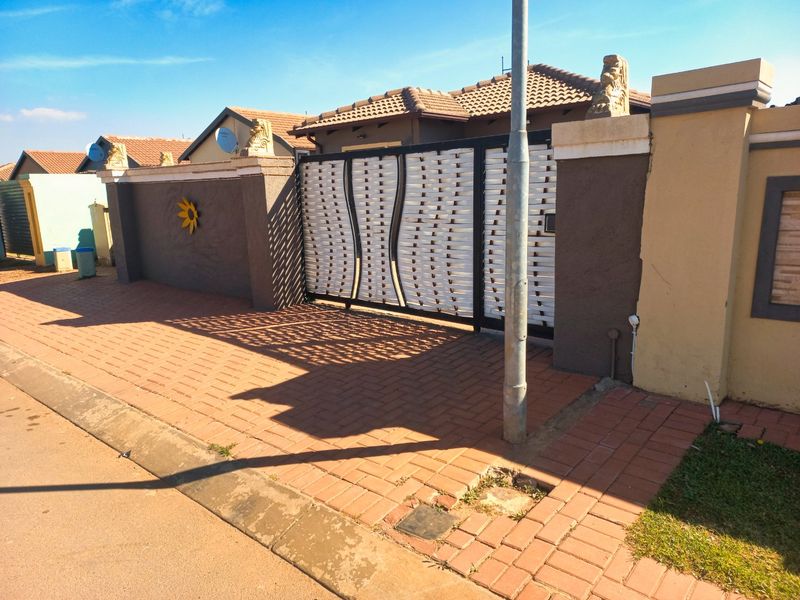 Front view of the property featuring a secure sliding gate, boundary wall with decorative pillars, and paved driveway access.