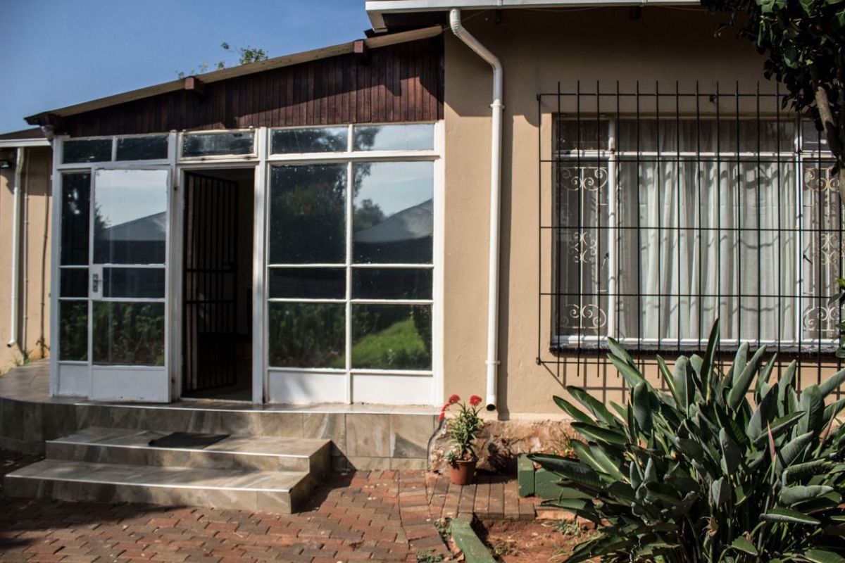 Rear exterior view featuring a tiled patio area, brick paving, and security bars on the windows.
