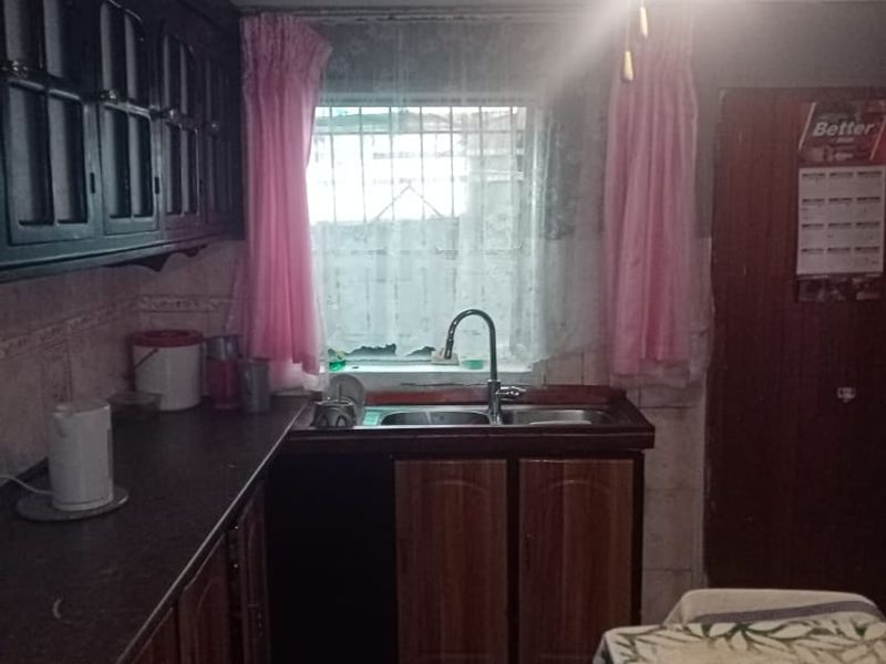 A dated kitchen featuring dark built-in cabinetry, a double basin sink, tiled flooring, and a ceiling fan, offering potential for modernization.