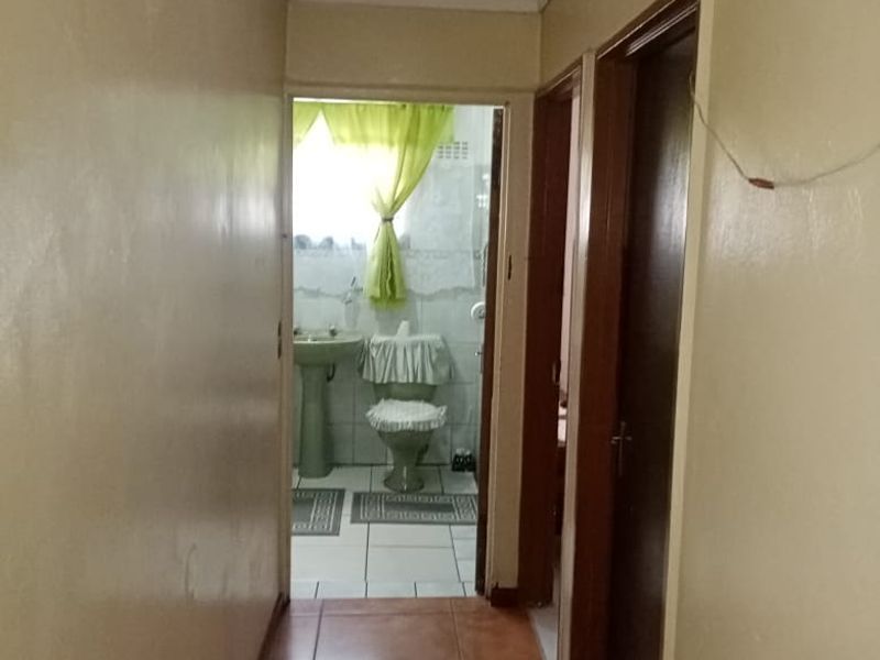 A functional hallway with tiled flooring leading towards a bathroom, featuring neutral wall finishes and standard internal door access.