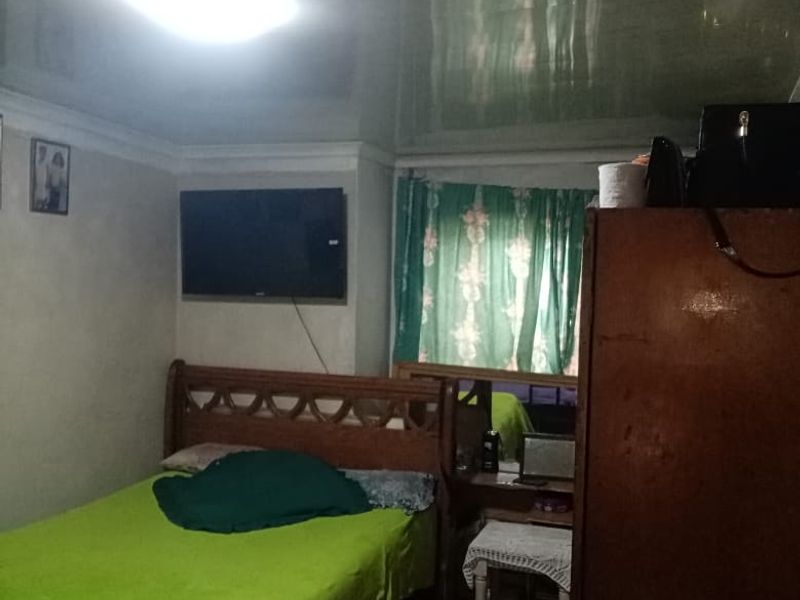 A bedroom featuring a glossy stretch ceiling with integrated lighting and tiled flooring, offering a functional space in need of cosmetic updates.