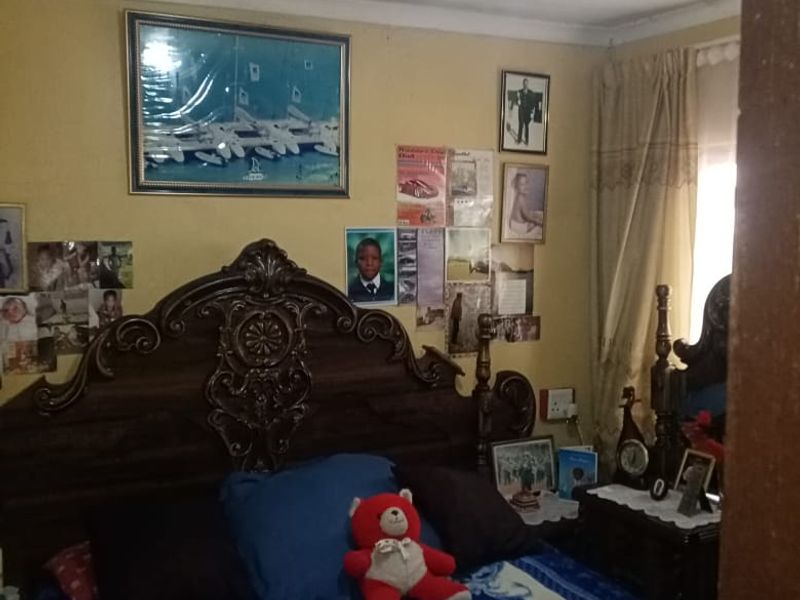 A bedroom featuring a large ornate headboard, curtain rails, and visible ceiling damage requiring maintenance and cosmetic updates.
