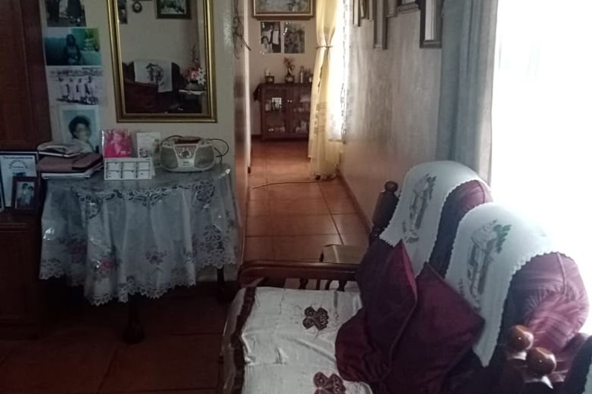 A living area featuring tiled flooring and an arched doorway leading to a hallway, providing a traditional layout with natural light.