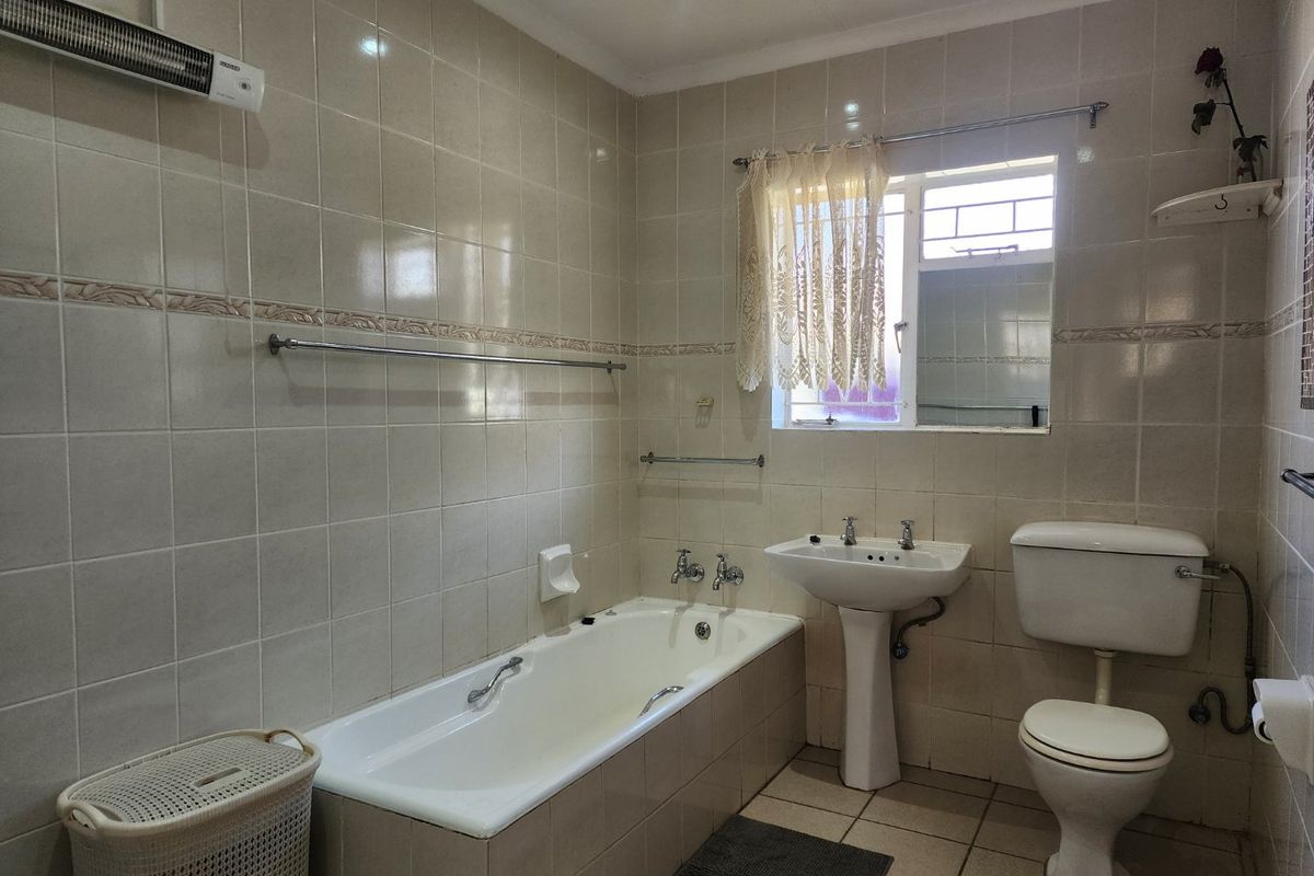 A functional bathroom featuring a built-in bathtub, pedestal washbasin, toilet, and wall-mounted heater, finished with neutral ceramic wall and floor tiles.