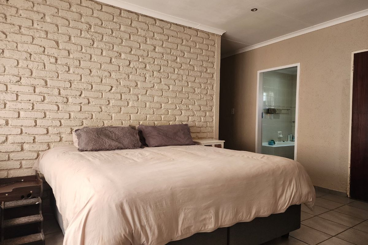 Spacious bedroom featuring a textured exposed brick feature wall, tiled flooring, and direct access to an en-suite bathroom.