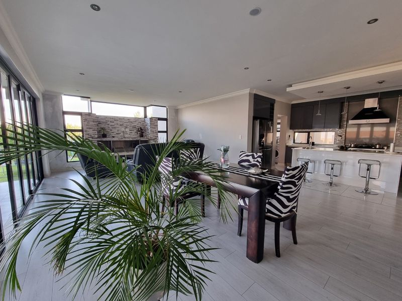 Spacious open-plan living area featuring a modern kitchen with island, stone feature wall with fireplace, and large stacking doors leading to the outdoors.