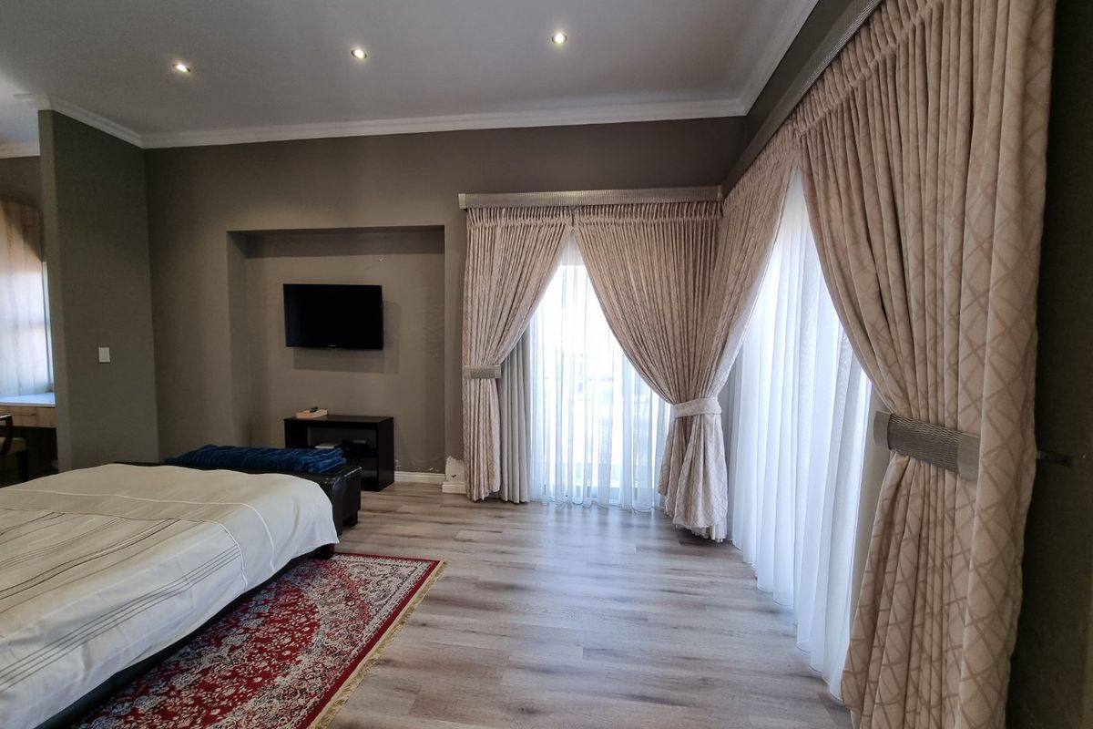 Spacious bedroom featuring modern laminate flooring, recessed ceiling lighting, and large floor-to-ceiling curtains leading to an outdoor area.