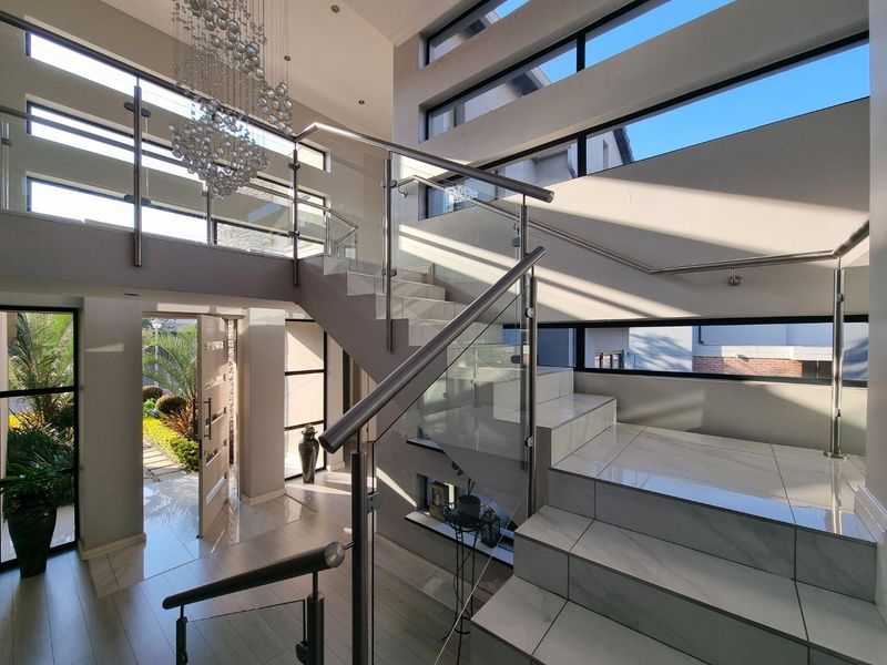 Spacious double-volume entrance hall featuring a modern tiled staircase with glass balustrades, large clerestory windows, and a contemporary pivot front door.