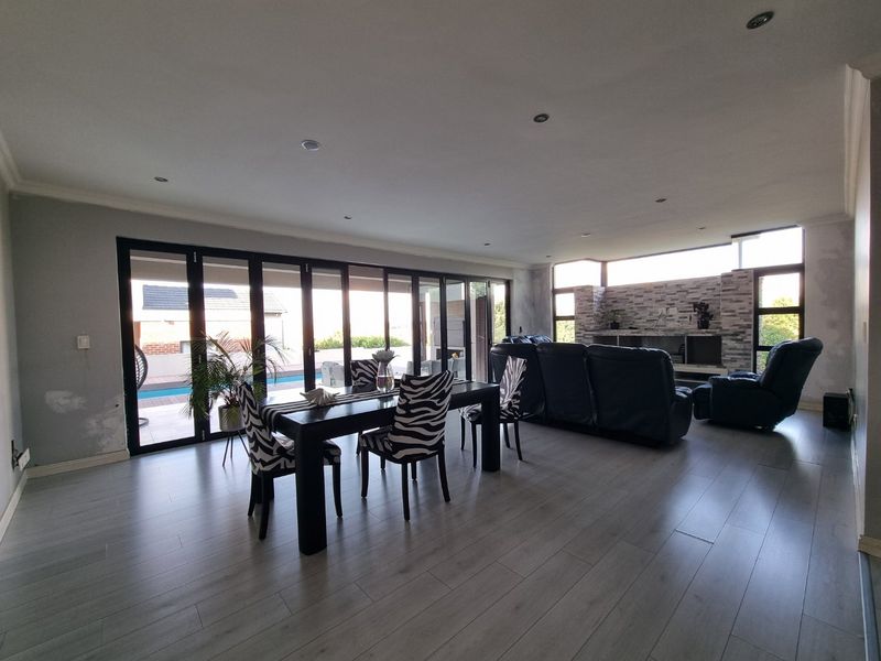 Spacious open-plan living and dining area featuring laminate flooring, a stone-clad feature wall with fireplace, and large stacking doors opening to the pool area.