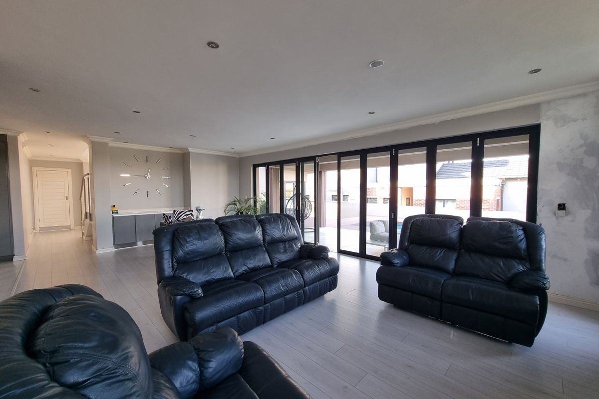 Spacious living area featuring modern laminate flooring, recessed lighting, and large bi-fold doors opening to the exterior, with some wall finishing required.