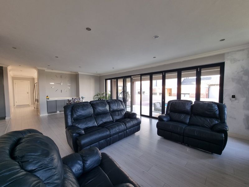 Spacious living area featuring modern laminate flooring, recessed lighting, and large bi-fold doors opening to the exterior, with some wall finishing required.