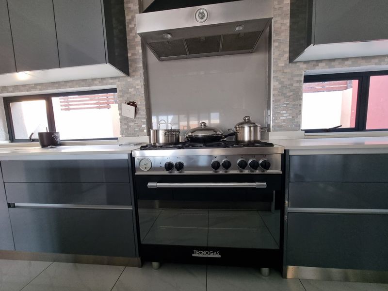 Modern kitchen featuring dark grey cabinetry, stone countertops, a stainless steel gas range with extractor fan, and a decorative tiled backsplash.