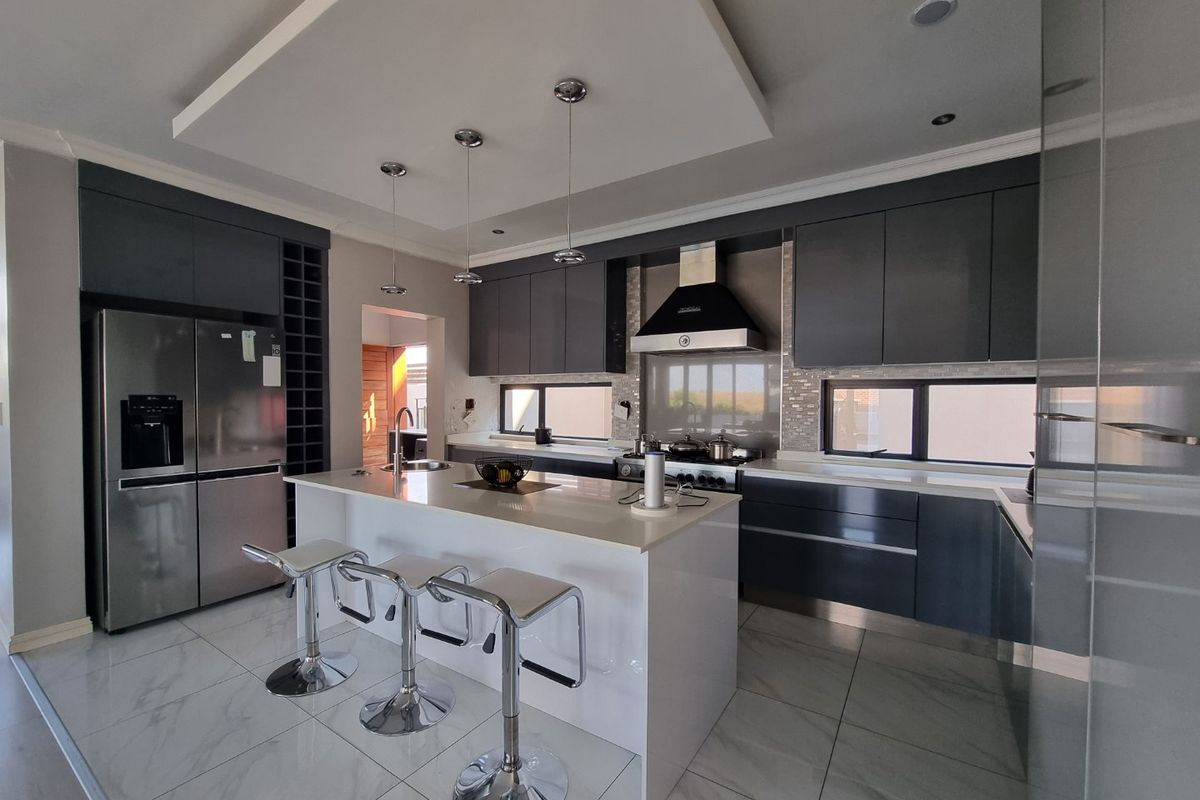 Modern kitchen featuring dark cabinetry, a central island with quartz countertops, high-end appliances, and sleek tiled flooring.