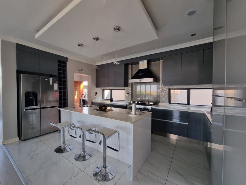 Modern kitchen featuring dark cabinetry, a central island with quartz countertops, high-end appliances, and sleek tiled flooring.