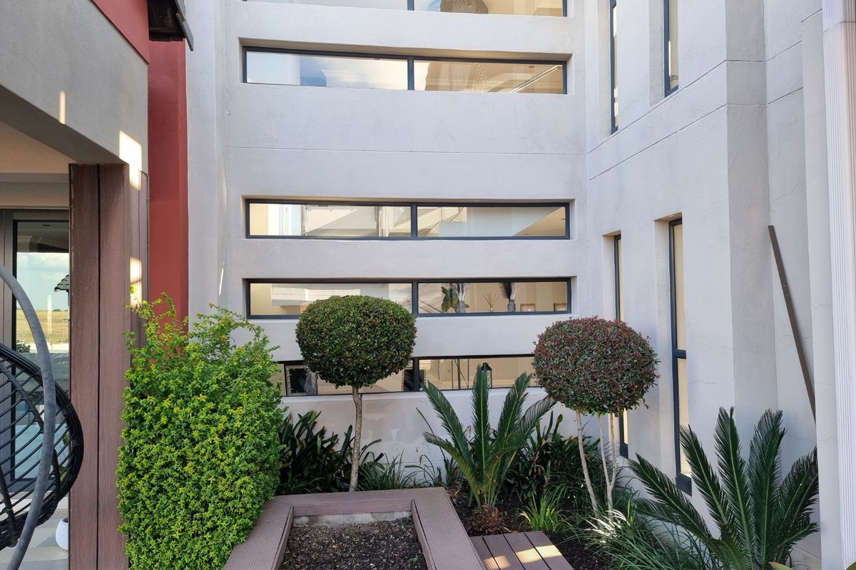 A modern rear courtyard featuring composite decking, a raised garden bed, and multiple horizontal strip windows providing natural light to the interior.