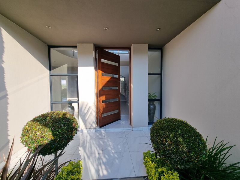 Modern entrance featuring a large timber pivot front door with glass sidelights and clean tiled flooring under a covered porch.