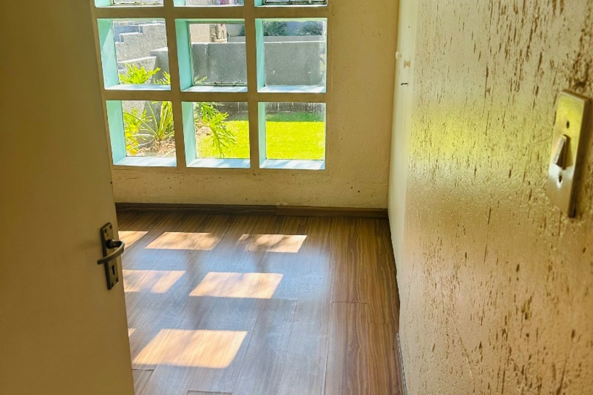 An empty bedroom featuring wood-look laminate flooring, textured walls, and a distinctive grid-style window providing natural light.
