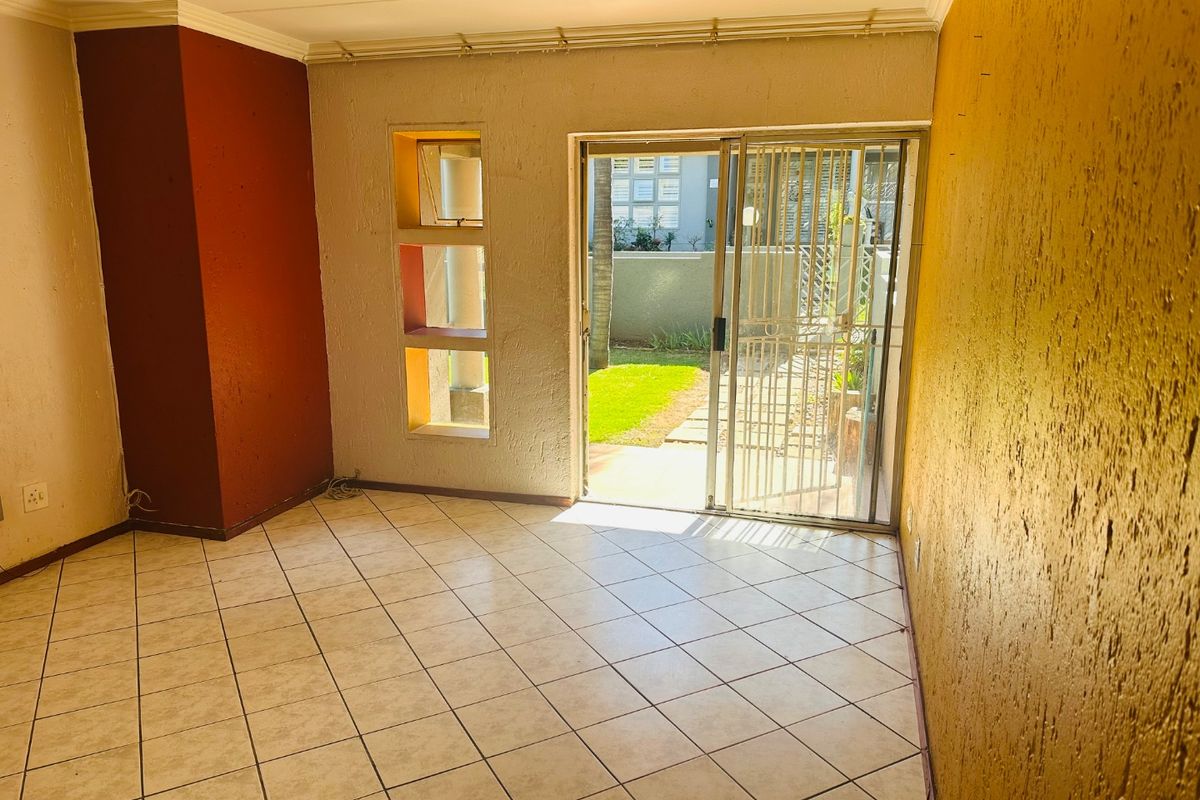 An empty living room featuring tiled floors, textured walls with accent colors, and a sliding glass door providing access to the garden.
