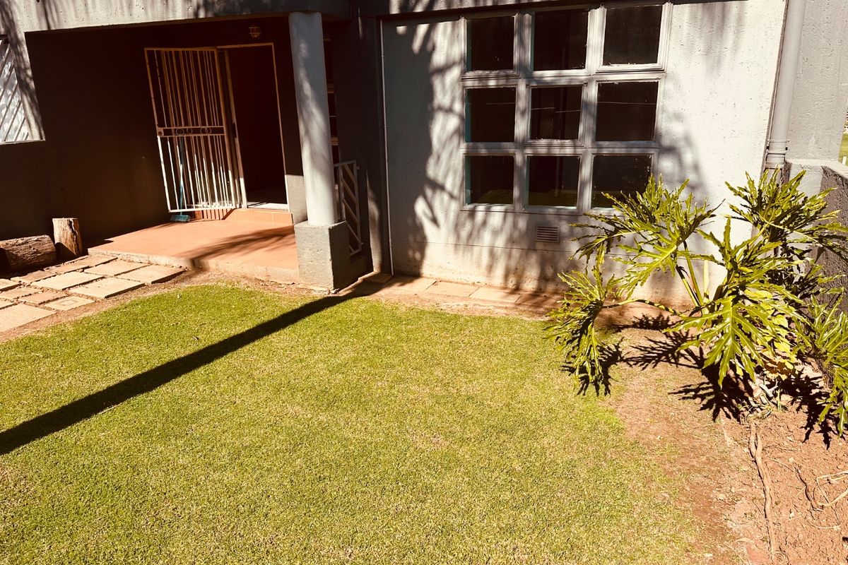 Rear exterior view featuring a small lawn, paved area, covered patio with security gate, and grid-style windows.