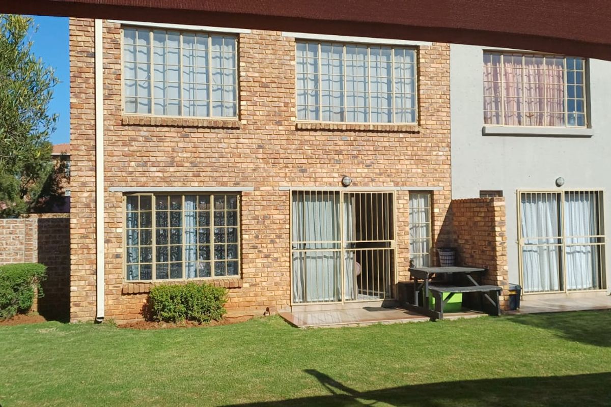 Rear view of a face brick apartment building featuring a private garden, paved patio area, and secure sliding door access.
