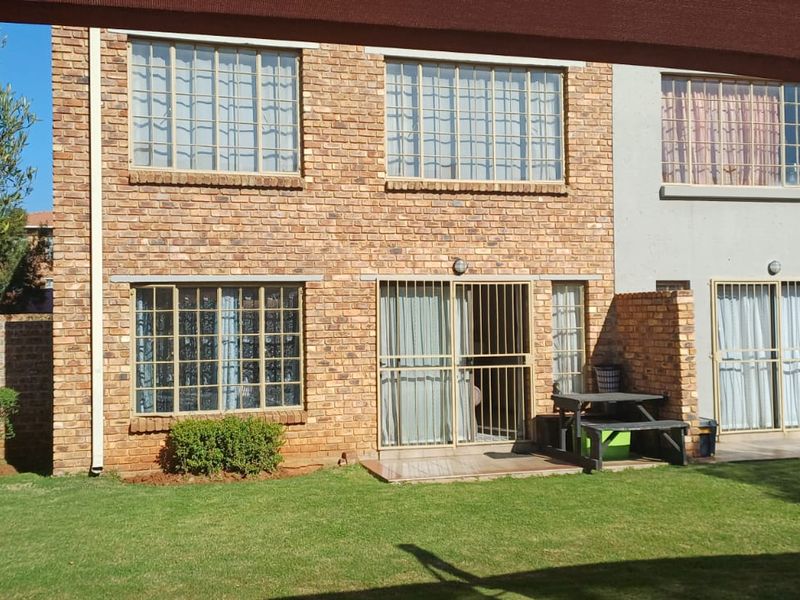 Rear view of a face brick apartment building featuring a private garden, paved patio area, and secure sliding door access.