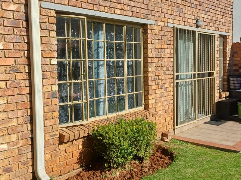 Rear exterior view of the apartment featuring a face brick facade, paved patio area, and access via a sliding door with security bars.