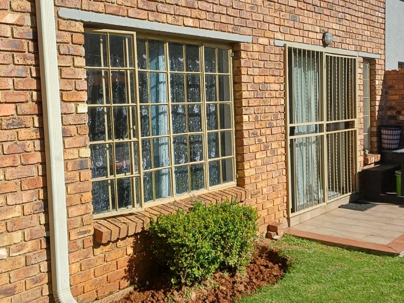 Rear exterior view of the apartment featuring a face brick facade, paved patio area, and access to a private garden space.