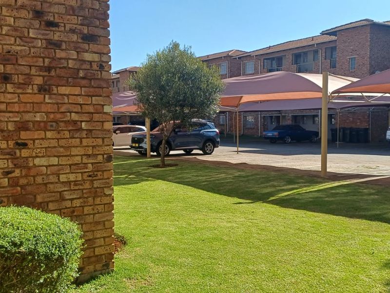 Exterior view of the apartment complex featuring face brick buildings, a well-maintained lawn, and covered parking bays for residents.