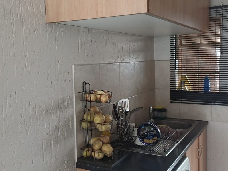 A compact kitchen area featuring built-in cabinetry, a tiled backsplash, and a stainless steel sink, with direct access to an outdoor area via a security gate.