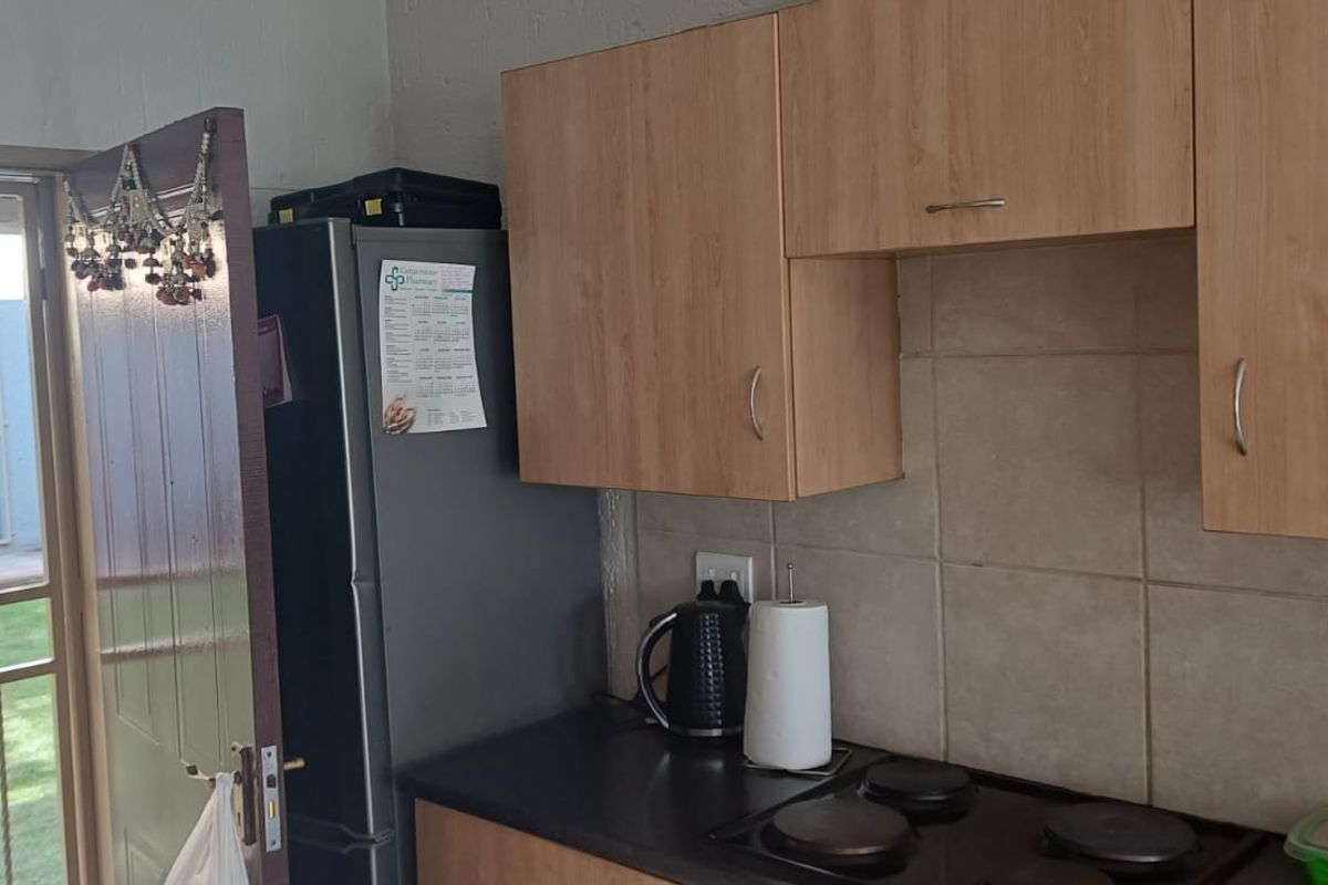 A functional kitchen area featuring built-in cabinetry, a tiled backsplash, and an electric hob, with direct access to an outdoor garden area.