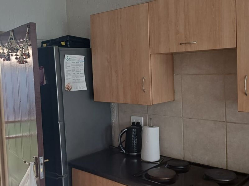 A functional kitchen area featuring built-in cabinetry, a tiled backsplash, and an electric hob, with direct access to an outdoor garden area.