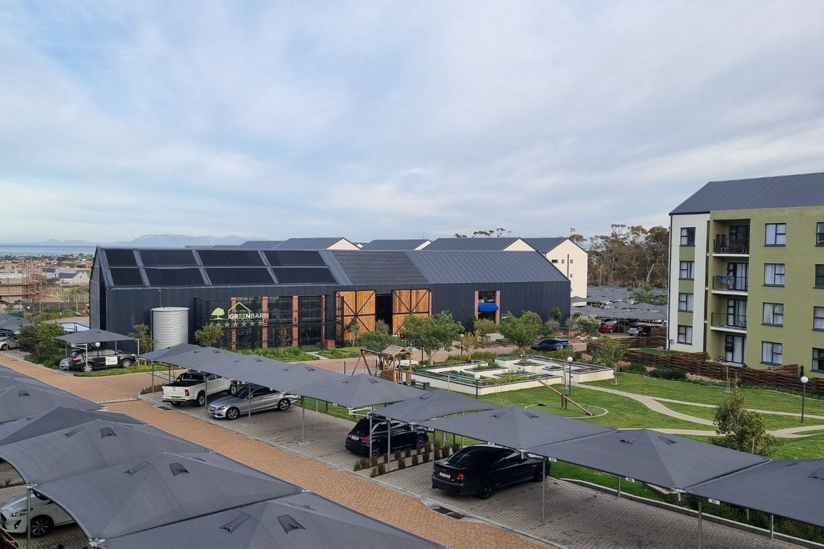 Aerial view of the apartment complex grounds, featuring covered parking bays, landscaped gardens, and a large communal building with solar panels.