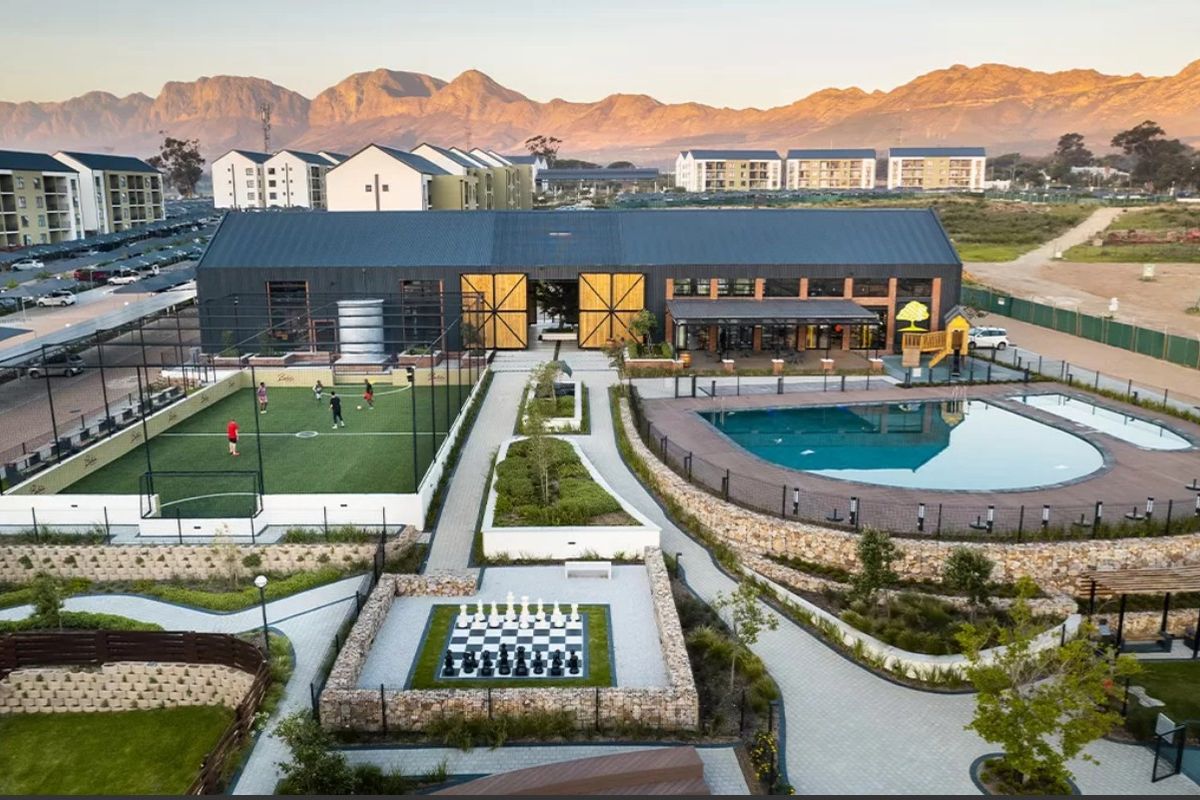Aerial view of a modern apartment complex featuring a swimming pool, sports court, clubhouse, and landscaped communal recreational areas with mountain views.