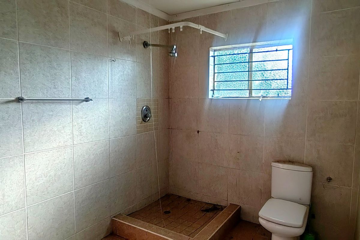 A functional bathroom featuring a walk-in shower with tiled surround, a standard toilet, and a window with security bars.