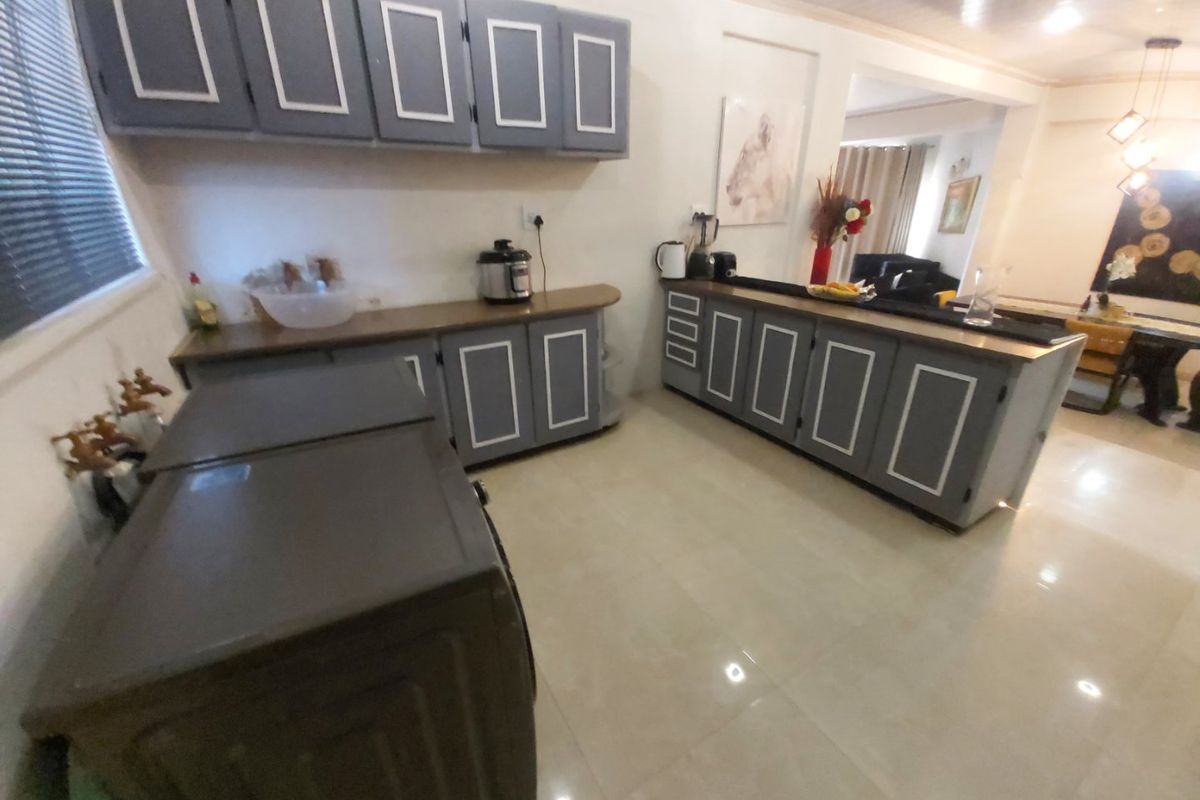 A functional kitchen featuring grey painted cabinetry with white trim, laminate countertops, and tiled flooring, flowing into an adjacent living and dining area.