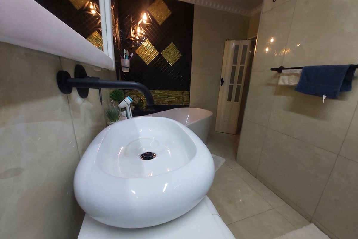 Modern bathroom featuring a white vessel sink with wall-mounted matte black faucet, tiled finishes, and a freestanding bathtub in the background.