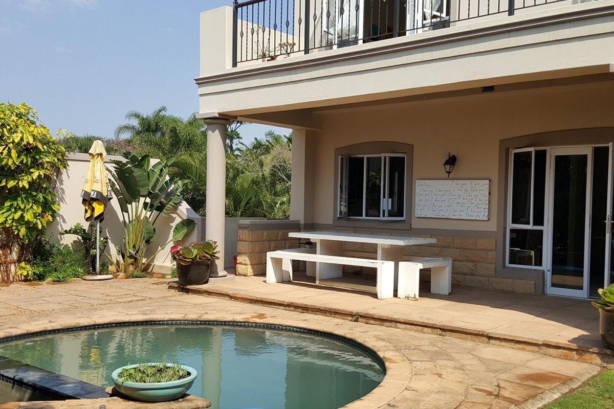 Outdoor pool area featuring stone paving, a covered patio space, and a balcony with wrought iron railings overlooking the garden.