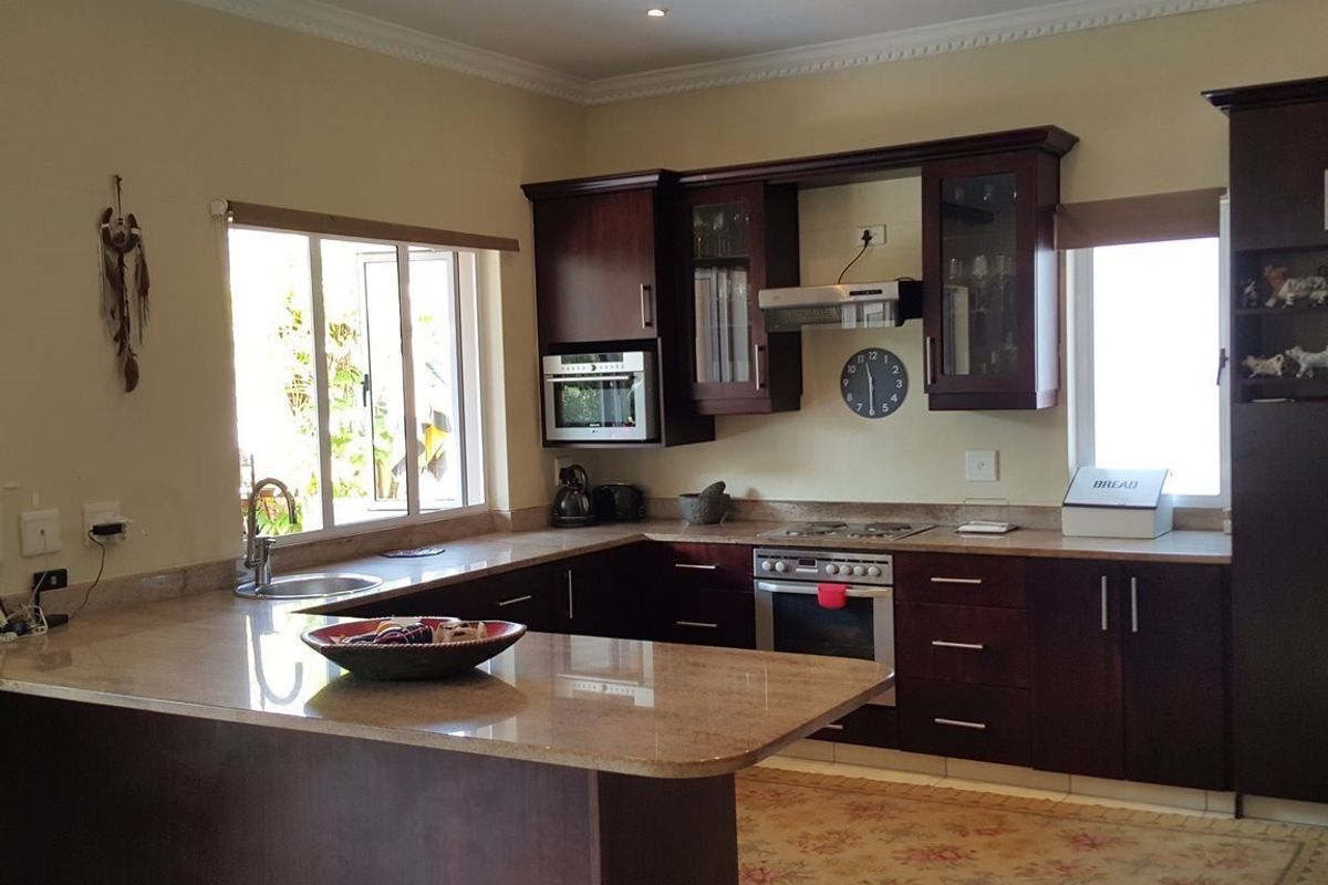 A functional kitchen featuring dark wood cabinetry, granite countertops, built-in oven, hob, and extractor fan with ample natural light.