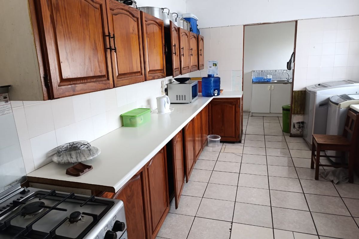 A functional kitchen featuring wooden cabinetry, laminate countertops, and a gas stove, with an adjoining scullery area and tiled flooring throughout.