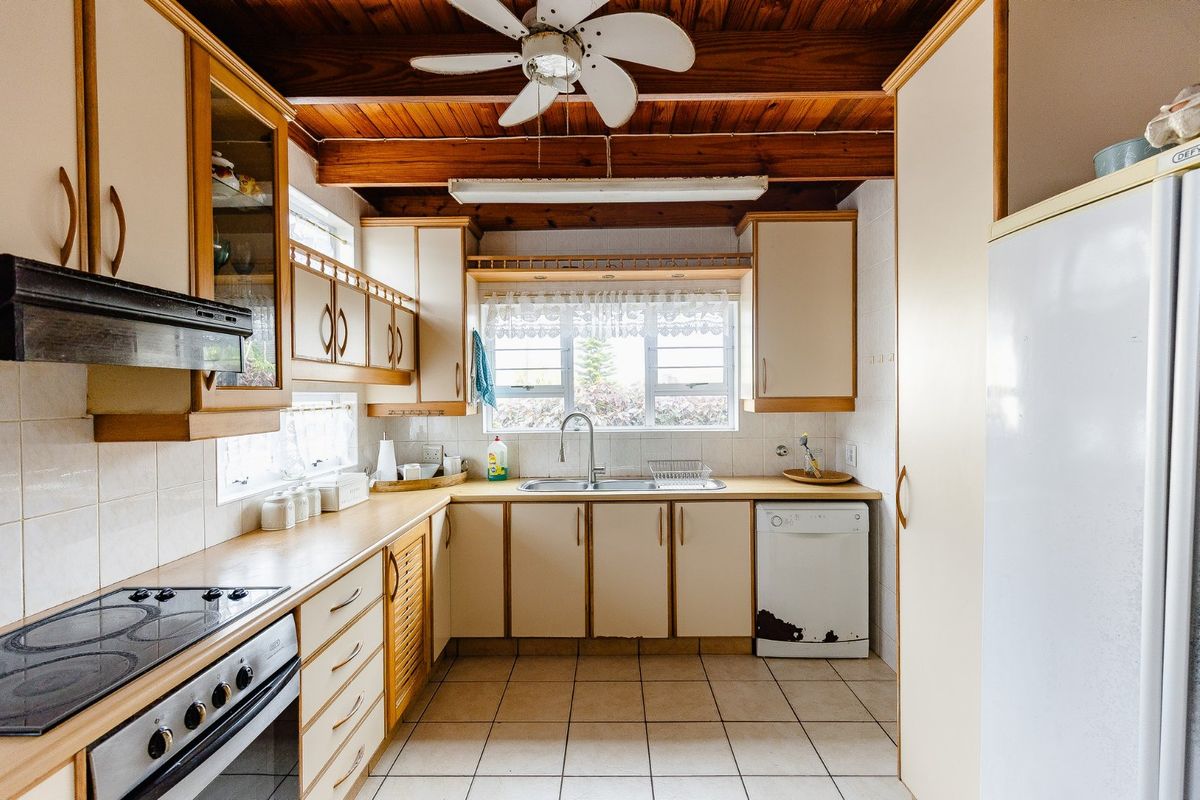 A functional kitchen featuring exposed timber ceiling beams, built-in cabinetry, tiled flooring, and a classic layout with integrated appliances.