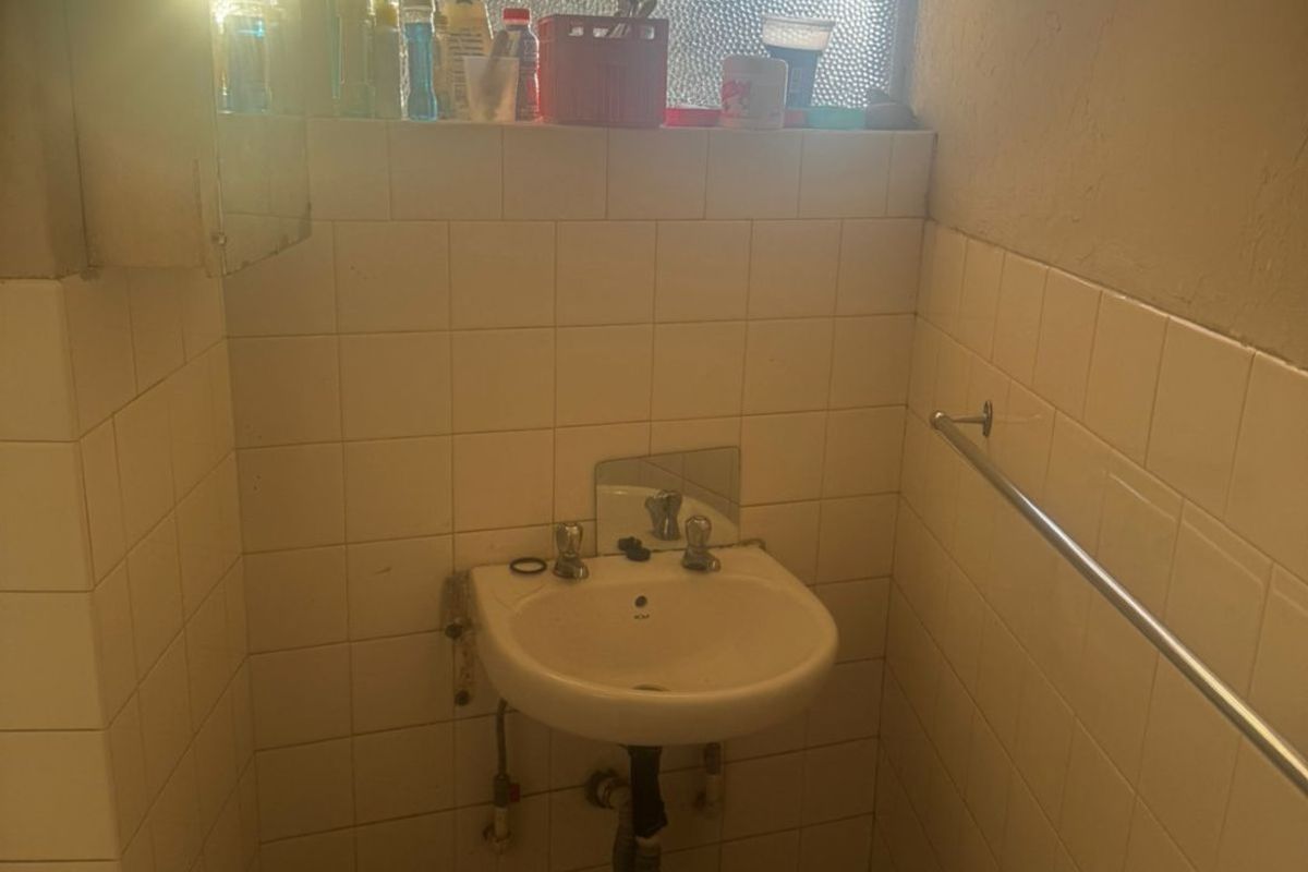 A dated bathroom featuring a wall-mounted basin, tiled splashback, and a towel rail, requiring cosmetic updates and plumbing maintenance.