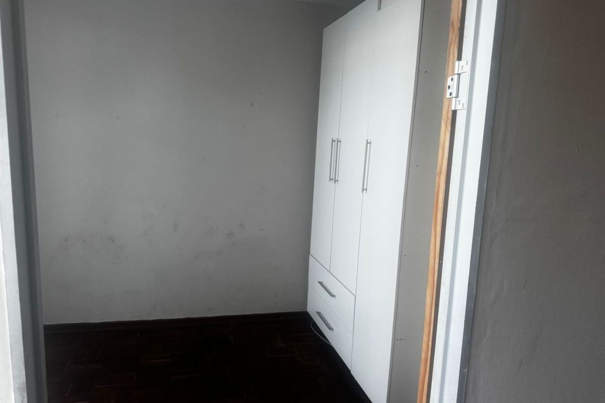 A compact bedroom featuring dark parquet flooring and a white built-in wardrobe, currently vacant and awaiting cosmetic updates.