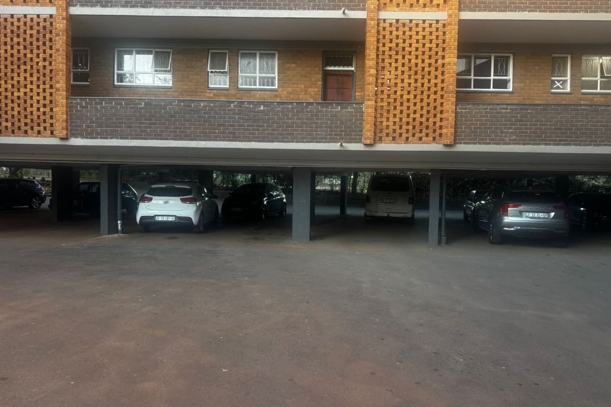 Covered ground-level parking area beneath an apartment building featuring brick masonry and concrete structural supports.