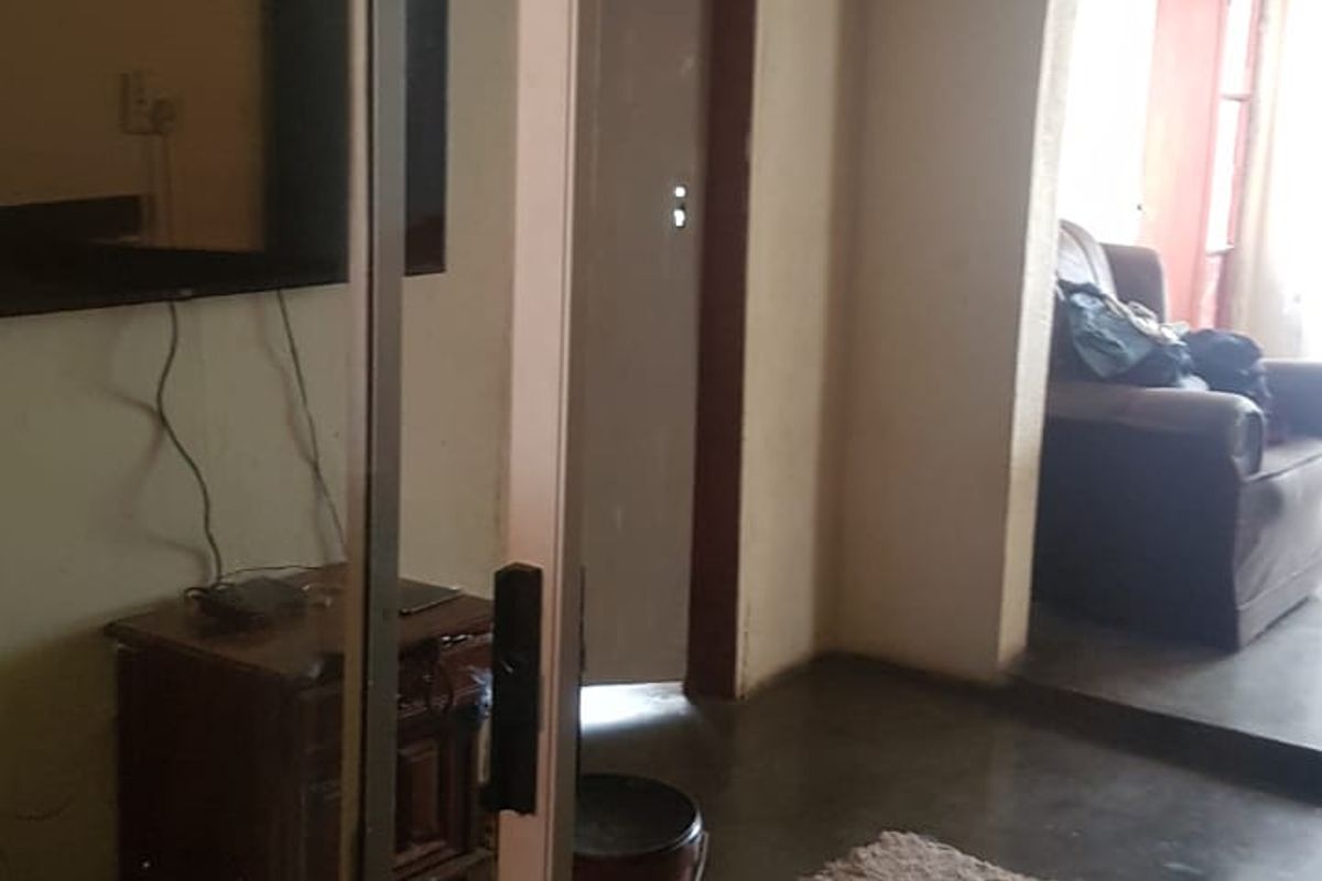 A living area featuring concrete flooring, an arched doorway, and a sliding glass door, showing signs of wear and requiring cosmetic updates.