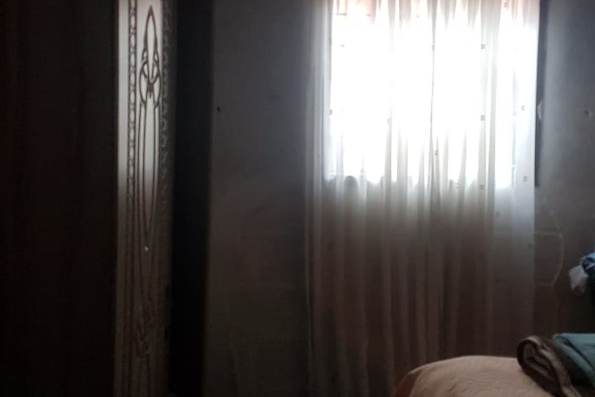 A dimly lit bedroom space featuring a window with curtains and basic wall finishes, requiring renovation to improve brightness and overall condition.